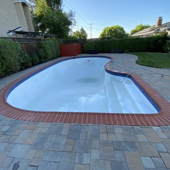 An empty, well-maintained swimming pool with a red brick edge and surrounding tiled patio in a backyard.